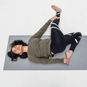 woman lying down in cat pulling its tail yoga pose